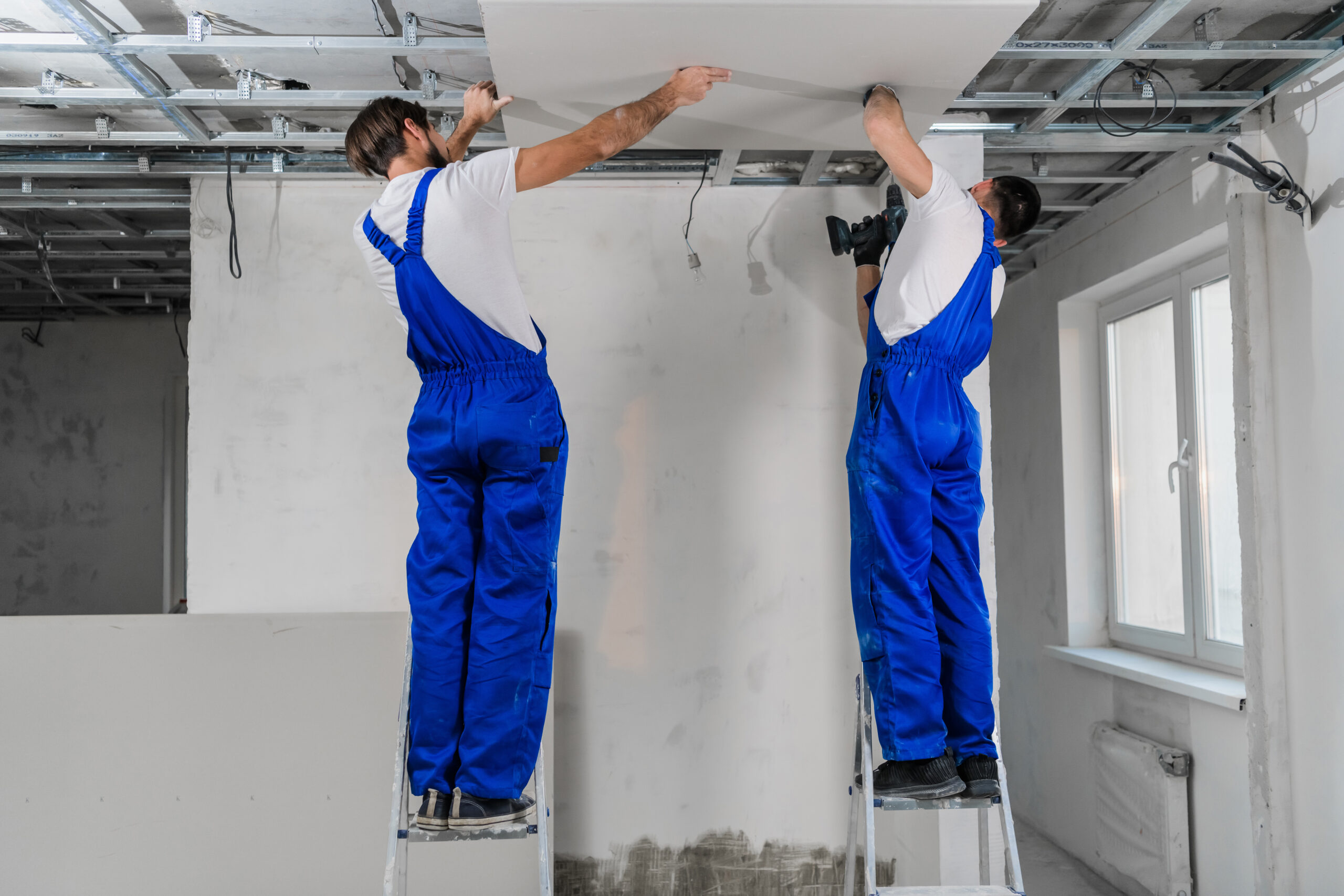 Men in blue overalls making ceiling in apartment room