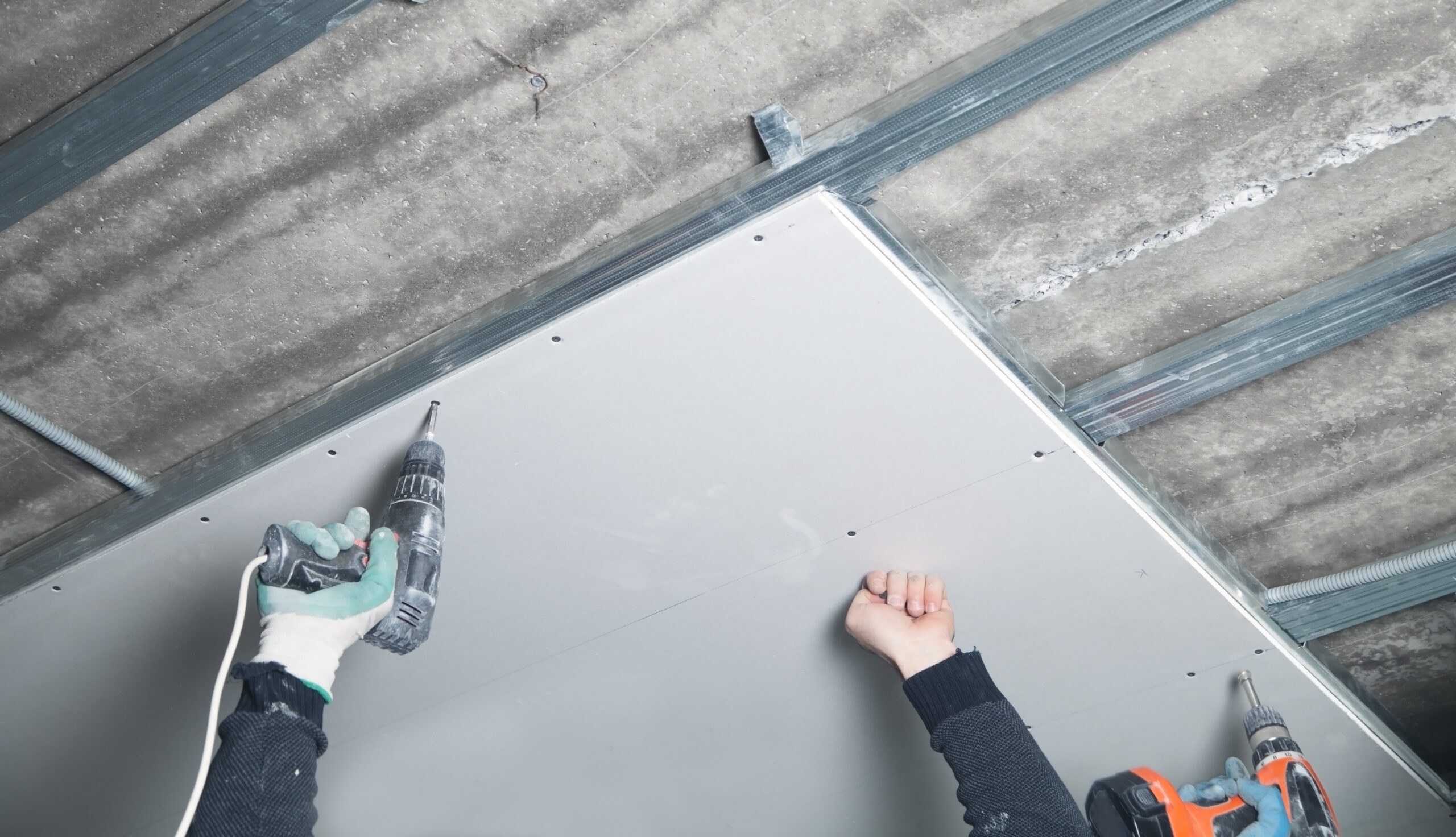 Worker with a drill screwdriver twists the screw into the drywal